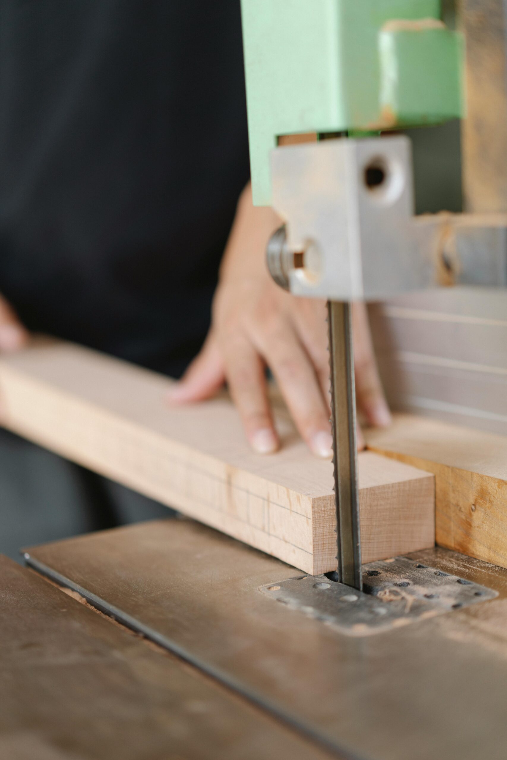 Crop anonymous artisan sawing wooden block using band saw with sharp blade in daylight